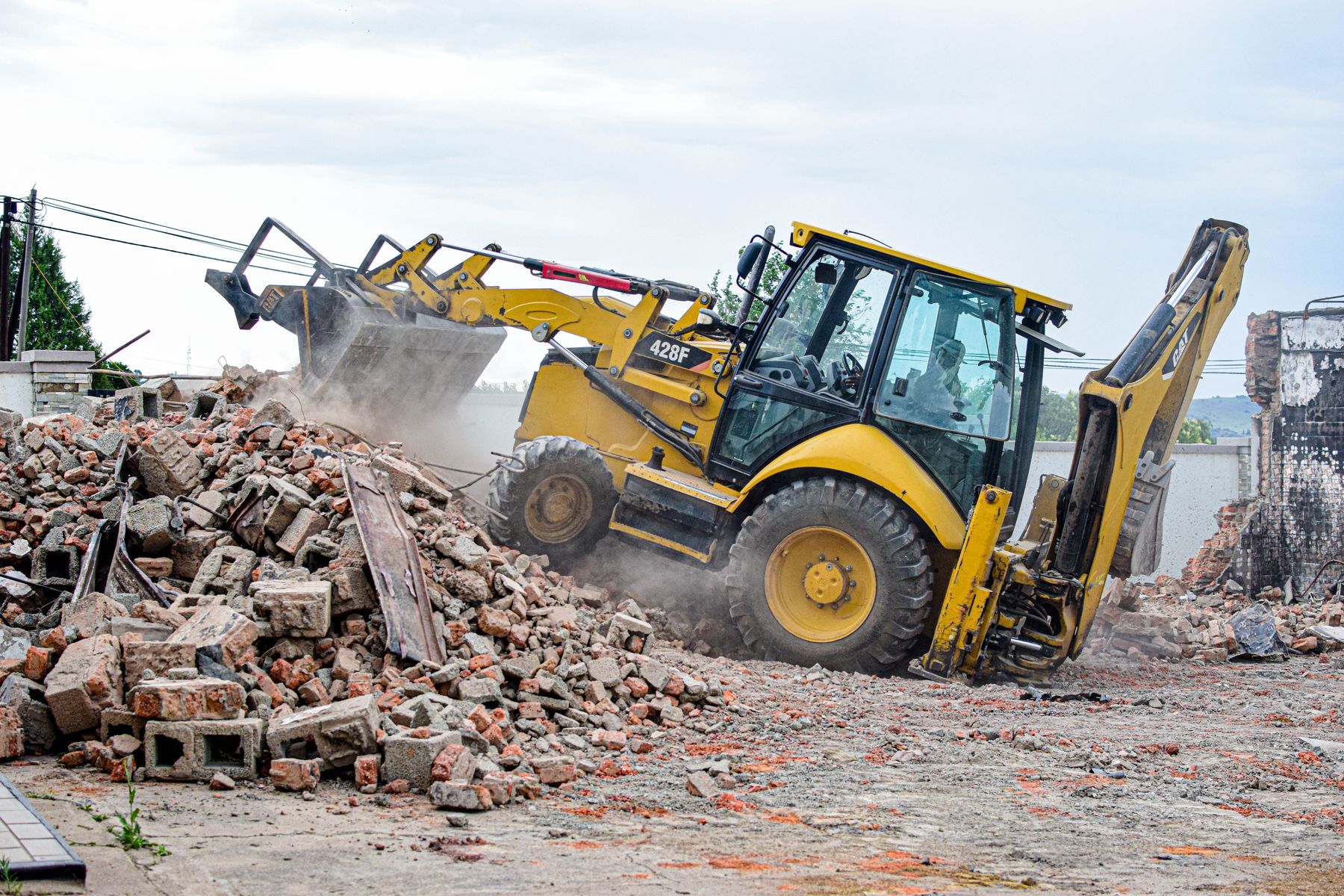 Nakladač nakládá stavební suť z demolice do kontejneru